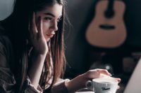 photo of woman lying on bed while using laptop